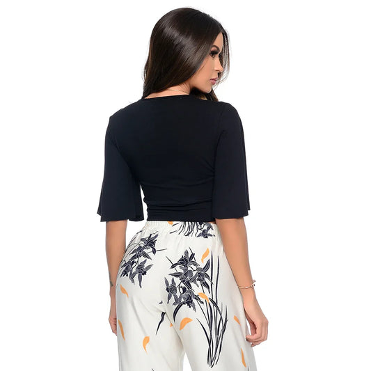 Mulher de costas com blusa preta e calça branca estampada com flores pretas e folhas laranja