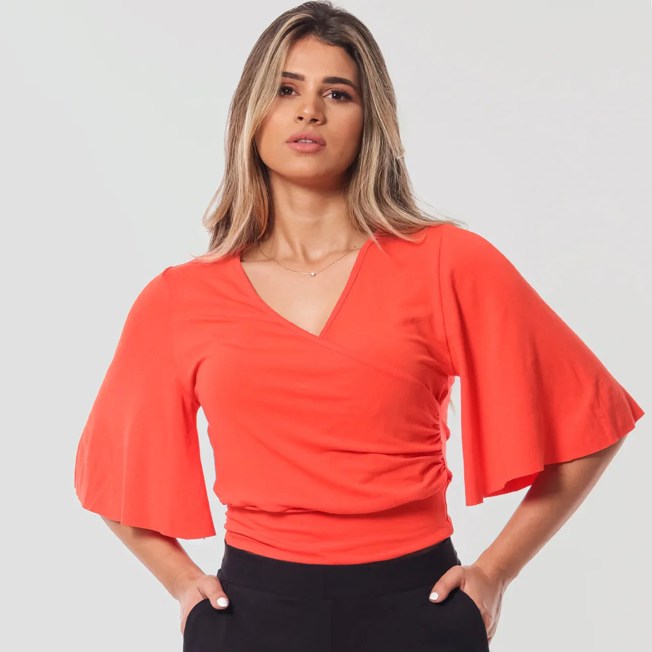 Mulher com blusa laranja manga ampla e calça preta posando com mãos nos bolsos