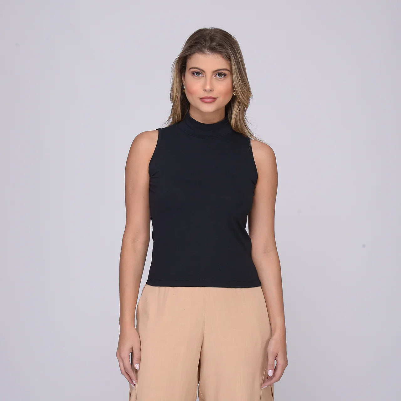 Mulher vestindo regata preta gola alta sem mangas com calça bege em fundo cinza claro