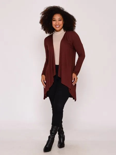 Mulher sorridente com cardigan vinho, blusa bege, calça preta e botas pretas em fundo claro