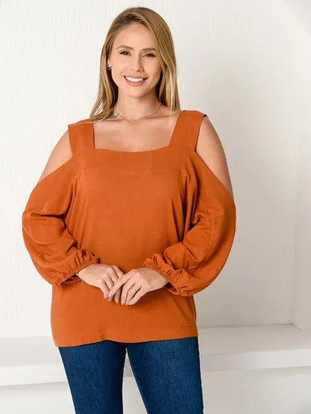 Mulher sorridente usando blusa laranja de mangas bufantes e recortes nos ombros, calça jeans azul