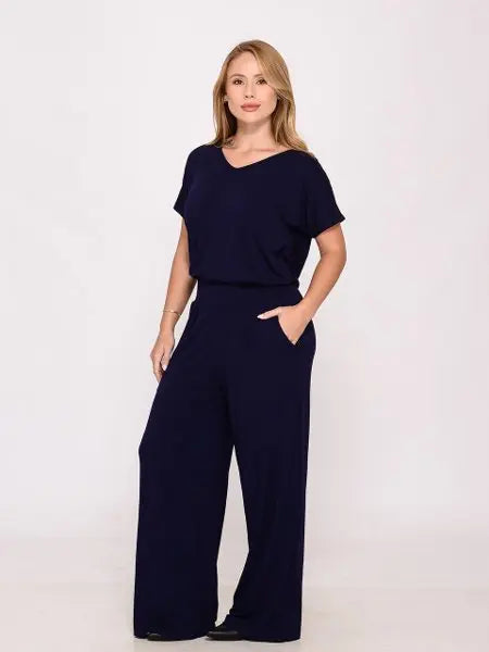 Mulher loira usando macacão azul marinho de manga curta e calça larga em estúdio branco