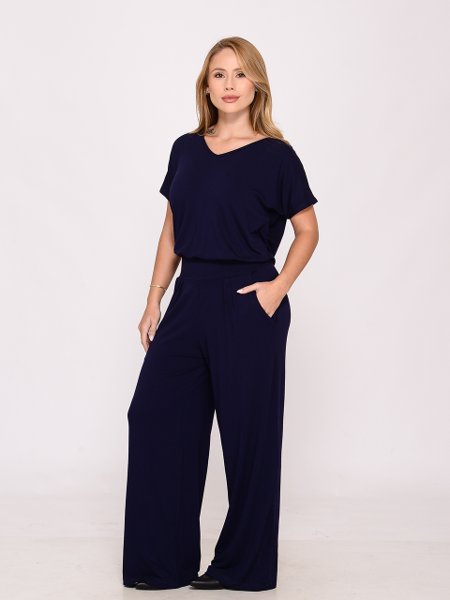 Mulher loira usando macacão azul marinho de manga curta e calça larga em estúdio branco