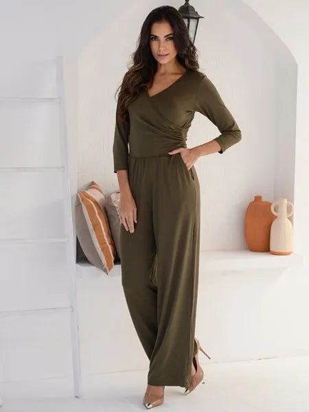 Mulher vestindo macacão verde musgo com mangas 3/4 em ambiente minimalista branco com almofadas e vasos