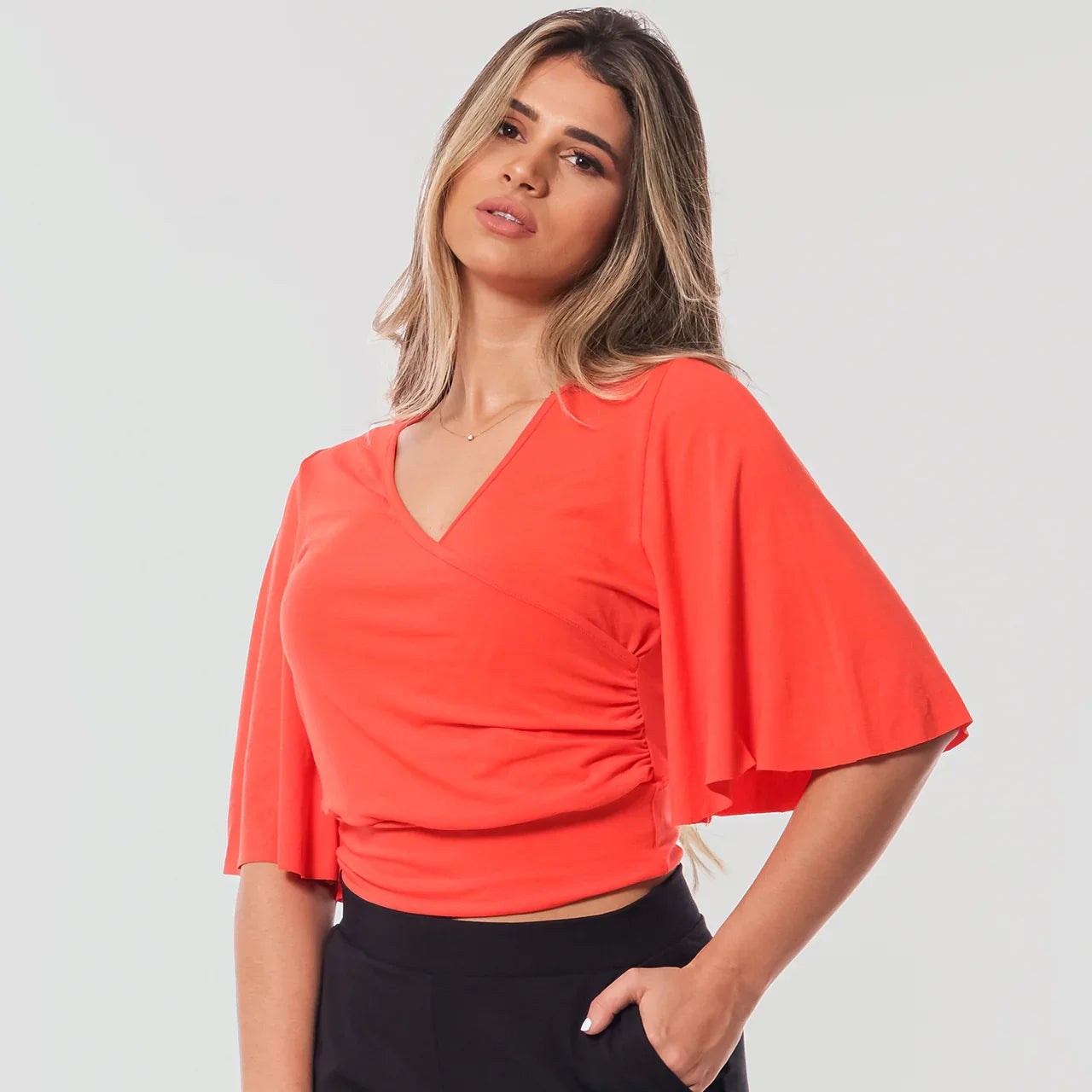 Mulher com blusa laranja de manga ampla e decote em V, com calça preta, fundo branco